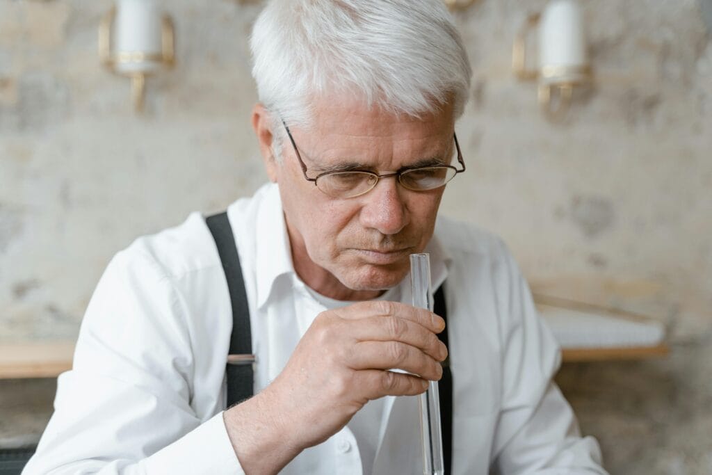 Elderly man analyzing scent from a test tube, focused on fragrance.